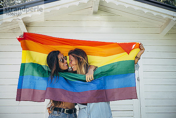 Zwei lächelnde Frauen halten eine Regenbogenfahne hoch