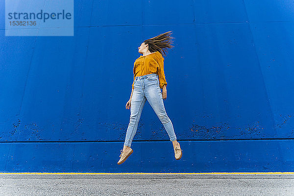 Junge Frau springt vor eine blaue Wand