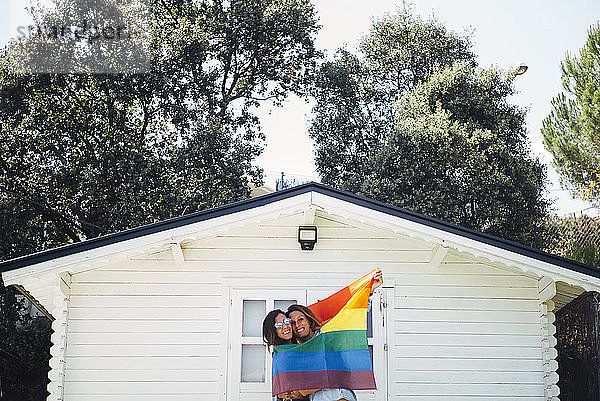 Zwei lächelnde Frauen halten eine Regenbogenfahne hoch