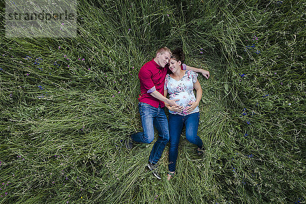 Schwangere Frau und Mann halten Babybauch,  liegen auf der Wiese