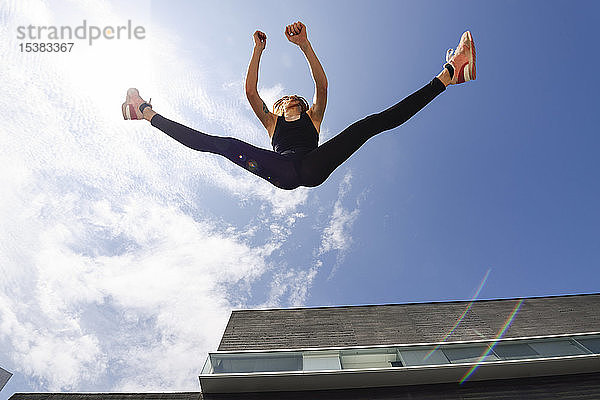 Sportliche junge Frau springt im Freien im Sonnenlicht