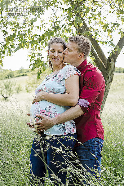 Schwangere Frau und Mann halten Babybauch,  Mann küsst seine Frau