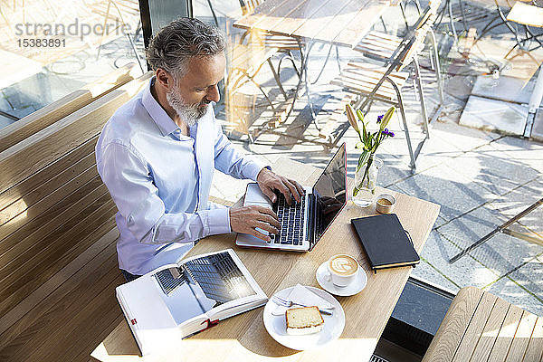 Reifer Mann mit Laptop in einem Café mit Buch auf dem Tisch