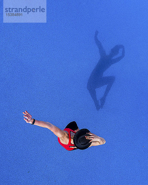 Springende junge Frau und ihr Schatten auf blauem Hintergrund,  Draufsicht