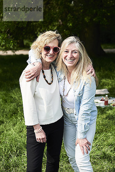 Porträt von zwei glücklichen Frauen,  die sich im Park umarmen