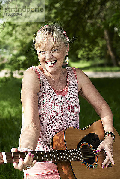 Porträt einer glücklichen älteren Frau,  die im Park Gitarre spielt