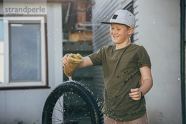 Glücklicher Junge reinigt bmx-Fahrrad auf dem Hof