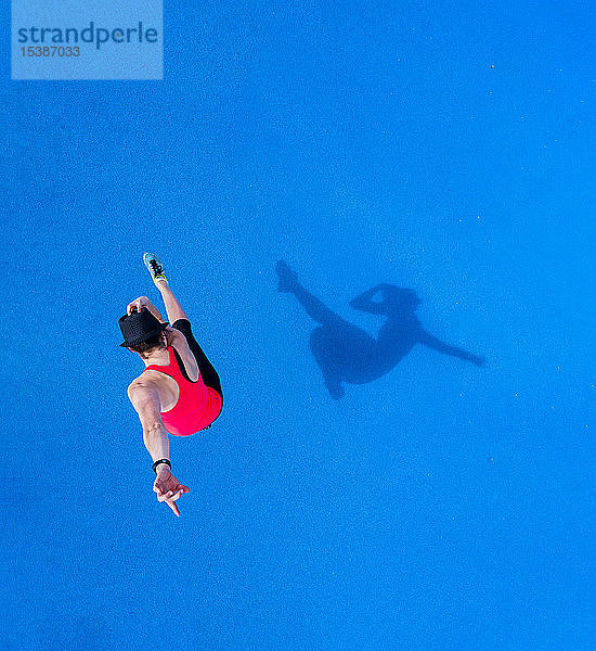 Springende junge Frau und ihr Schatten auf blauem Hintergrund,  Draufsicht