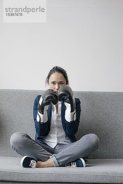 Porträt einer jungen Frau,  die auf einer Couch sitzt und Boxhandschuhe trägt
