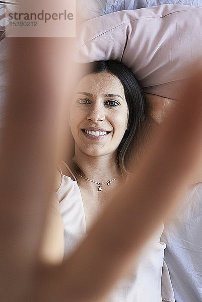 Porträt einer lächelnden,  auf dem Bett liegenden jungen Frau mit Siegeszeichen,  Draufsicht