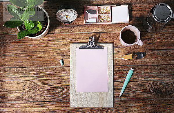 Klemmbrett mit rosa Blankopapier,  Kaffeetasse und anderen Utensilien auf dem Schreibtisch im Heimbüro,  Draufsicht