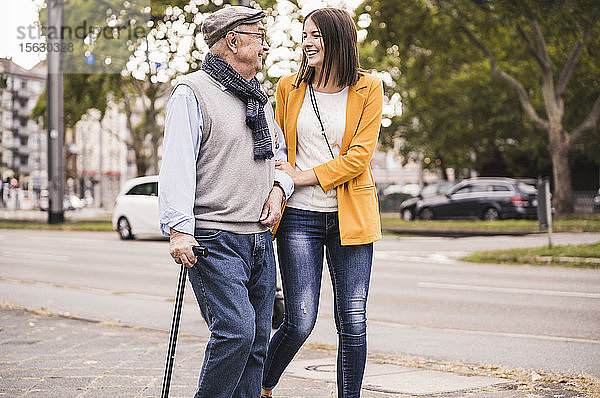 Erwachsene Enkelin hilft ihrem Großvater beim Spaziergang mit einem Spazierstock