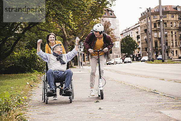 Älterer Mann im Rollstuhl vergnügt sich mit seinen erwachsenen Enkelkindern im Freien