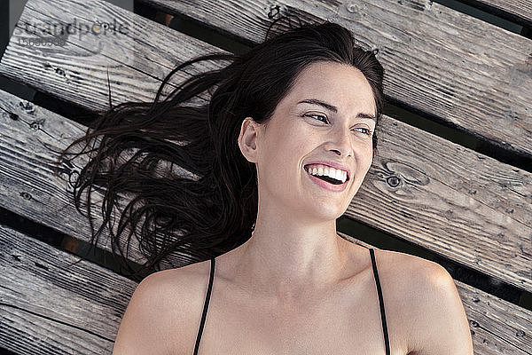 Porträt einer lachenden jungen Frau,  die sich auf einem Steg entspannt