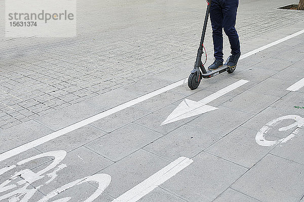 Beine eines Mannes,  der auf einem E-Scooter auf dem Fahrradweg in der Stadt fährt