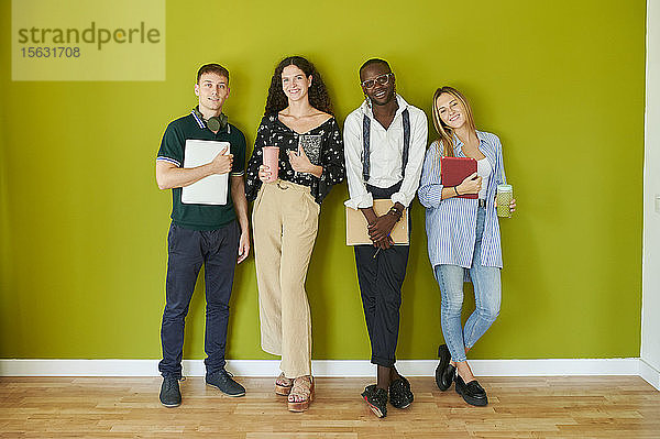 Porträt von lächelnden Gelegenheitskollegen,  die zusammen vor einer grünen Wand in einem modernen Büro stehen