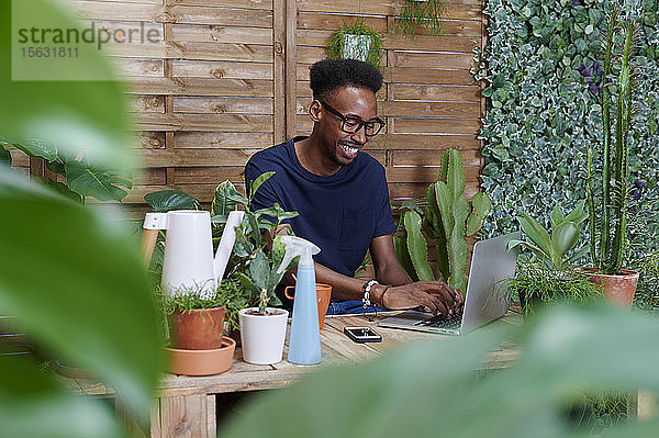 Lächelnder junger Mann mit Laptop auf seiner Terrasse