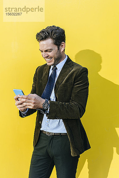 Glücklicher Geschäftsmann mit Smartphone vor gelber Wand