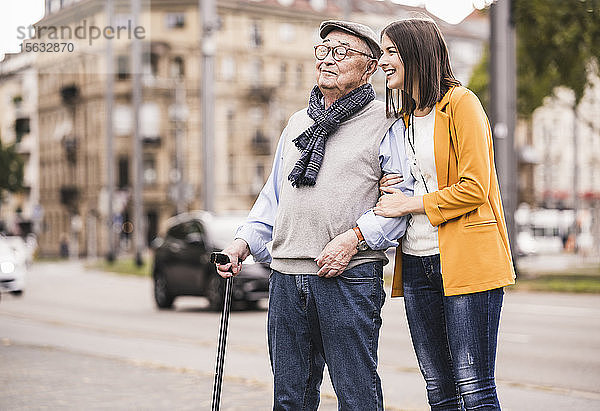 Erwachsene Enkelin hilft ihrem Großvater beim Spaziergang mit einem Spazierstock