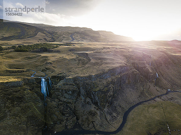 Island,  Luftaufnahme eines Wasserfalls,  der bei Sonnenuntergang von einer hohen Klippe herunterplätschert