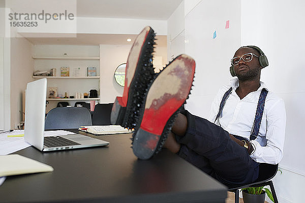Entspannter junger Geschäftsmann mit Kopfhörern am Schreibtisch im Büro sitzend