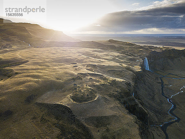 Island,  Luftaufnahme eines Wasserfalls,  der bei Sonnenuntergang von einer hohen Klippe herunterplätschert