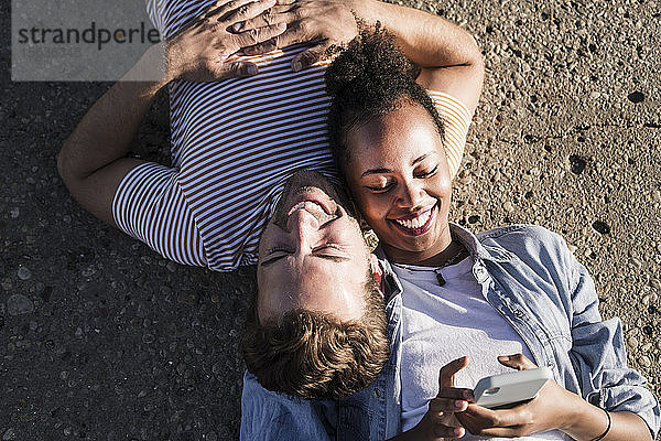 Glückliches junges Paar liegt auf Betonboden und benutzt Handy