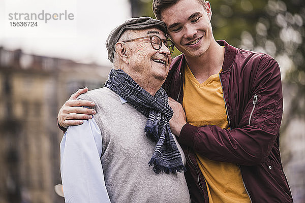 Glücklicher älterer Mann Kopf an Kopf mit seinem erwachsenen Enkel im Freien