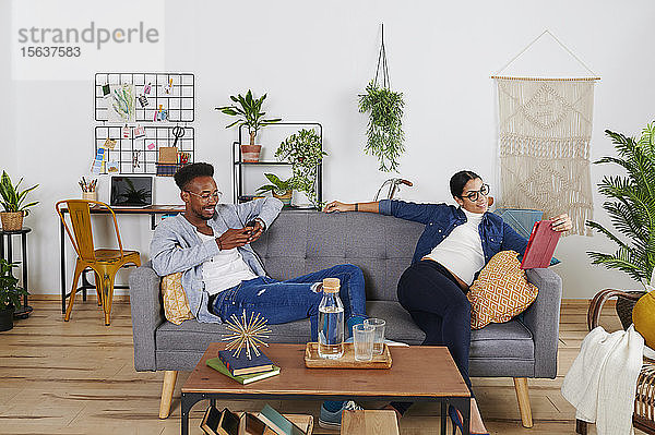Multiethnisches Paar verbringt Zeit zusammen im Wohnzimmer,  Frau mit Tablet und Mann mit Smartphone