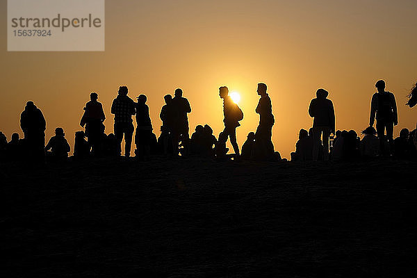 Portugal,  Algarve,  Silhouetten von Menschen,  die sich am Kap Saint Vincent gegen die untergehende Sonne entspannen