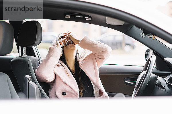 Lachende Geschäftsfrau mit Smartphone im Auto