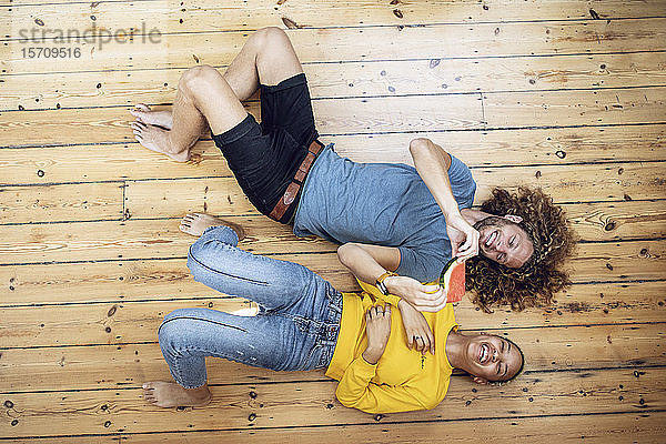 Glückliches junges Paar liegt zu Hause auf dem Boden und teilt sich eine Wassermelone
