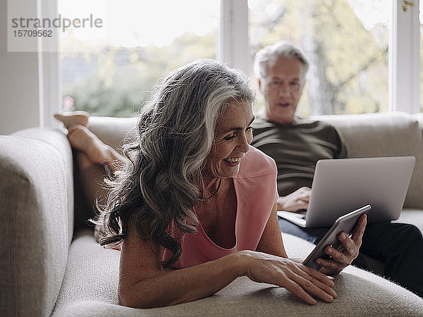 Älteres Ehepaar entspannt sich zu Hause auf der Couch mit Tablet und Laptop