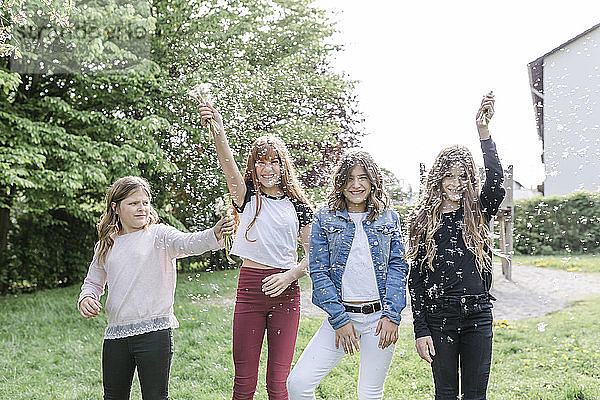 Vier glückliche Mädchen spielen mit Löwenzahnsamen