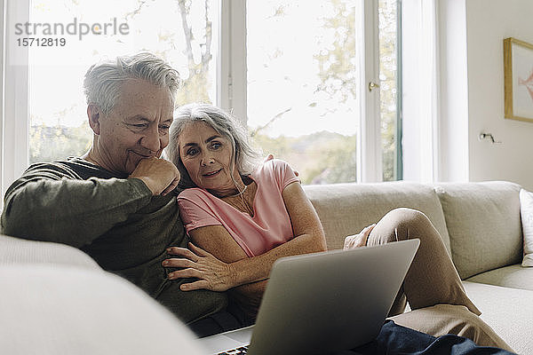 Älteres Ehepaar betrachtet Laptop auf der Couch zu Hause