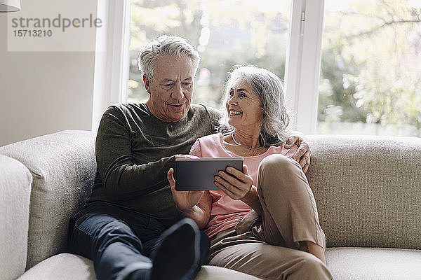 Glückliches älteres Ehepaar entspannt zu Hause auf der Couch mit Tablette