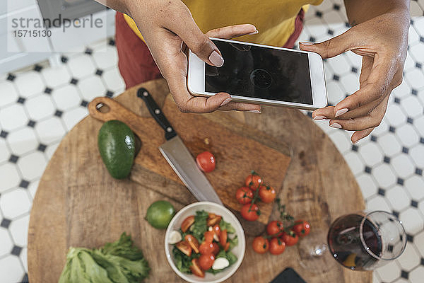 Nahaufnahme einer Frau in der Küche,  die eine gesunde Mahlzeit zubereitet und ein Smartphone in der Hand hält