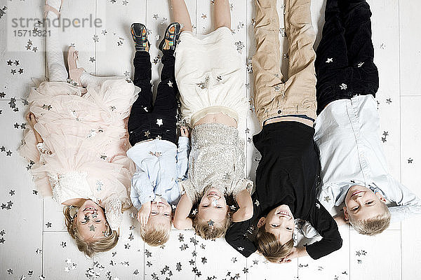 Gruppenbild von fünf Kindern,  die kopfüber auf dem Boden liegen und von Weihnachtskonfetti bedeckt sind