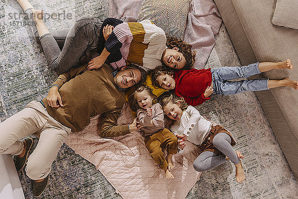Glückliche Familie mit drei Töchtern,  die zu Hause auf Decken liegen