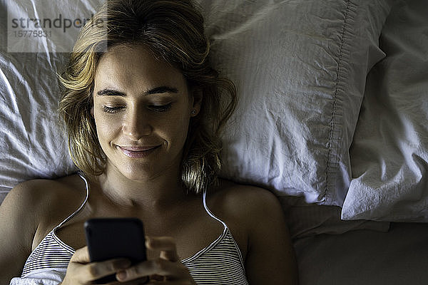 Junge Frau benutzt Smartphone auf dem Bett