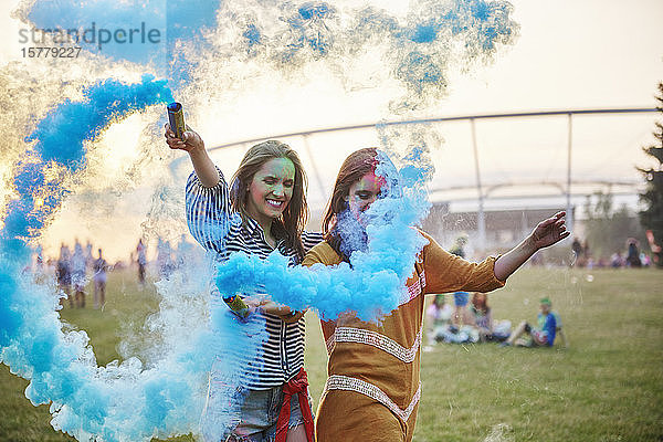 Zwei junge Frauen tanzen mit blauen Rauchbomben beim Holi-Festival