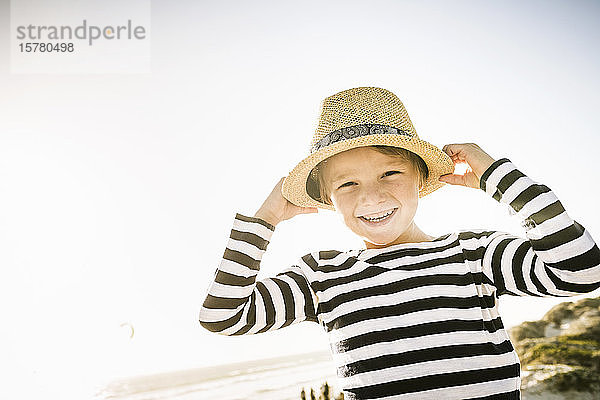 Porträt eines glücklichen Jungen mit Hut am Strand