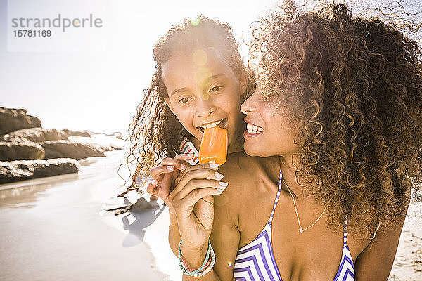 Frau und Tochter teilen sich am Strand ein Eis am Stiel