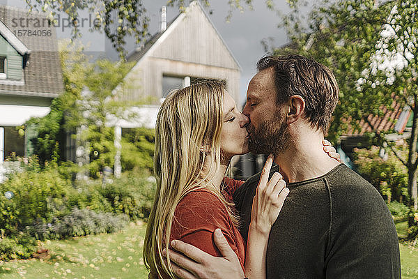 Glückliches Paar küsst sich im Garten,  vor ihrem Traumhaus
