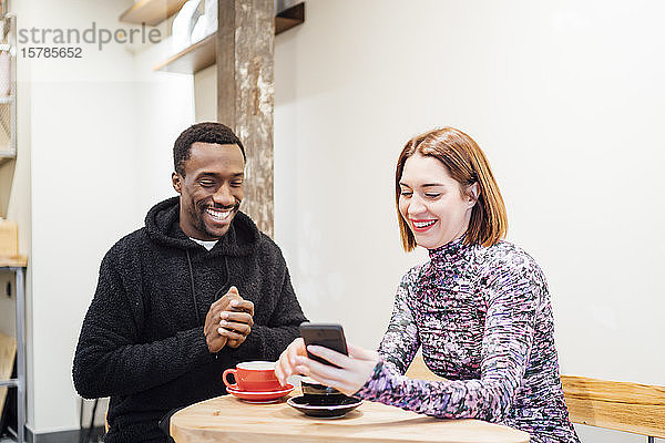 Lächelnder Mann und lächelnde Frau mit Handy in einem Cafe