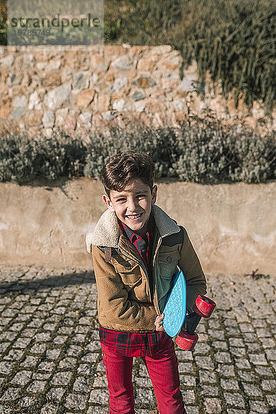 Porträt eines glücklichen Jungen mit Skateboard in der Hand