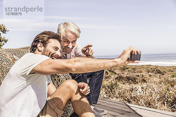 Vater und erwachsener Sohn amüsieren sich gemeinsam auf einer Terrasse am Meer