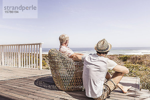 Vater und erwachsener Sohn sitzen auf einer Terrasse am Meer