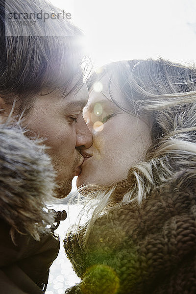 Küssendes junges Paar im Winter bei Gegenlicht