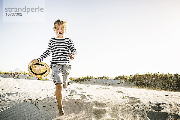 Glücklicher Junge mit Hut läuft am Strand